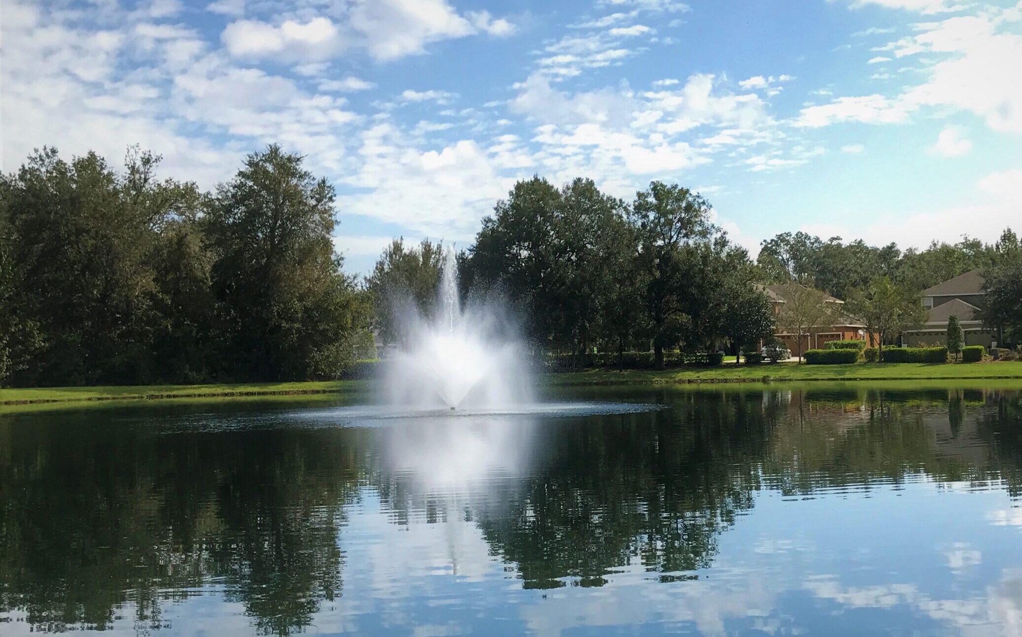 Small fountain sprays into the lake in a lakeside neighborhood.