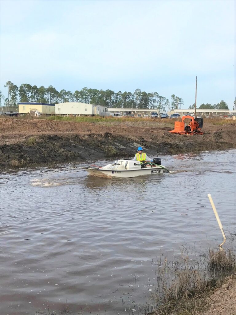 A man cleaning a very muddy body of water from a boat.